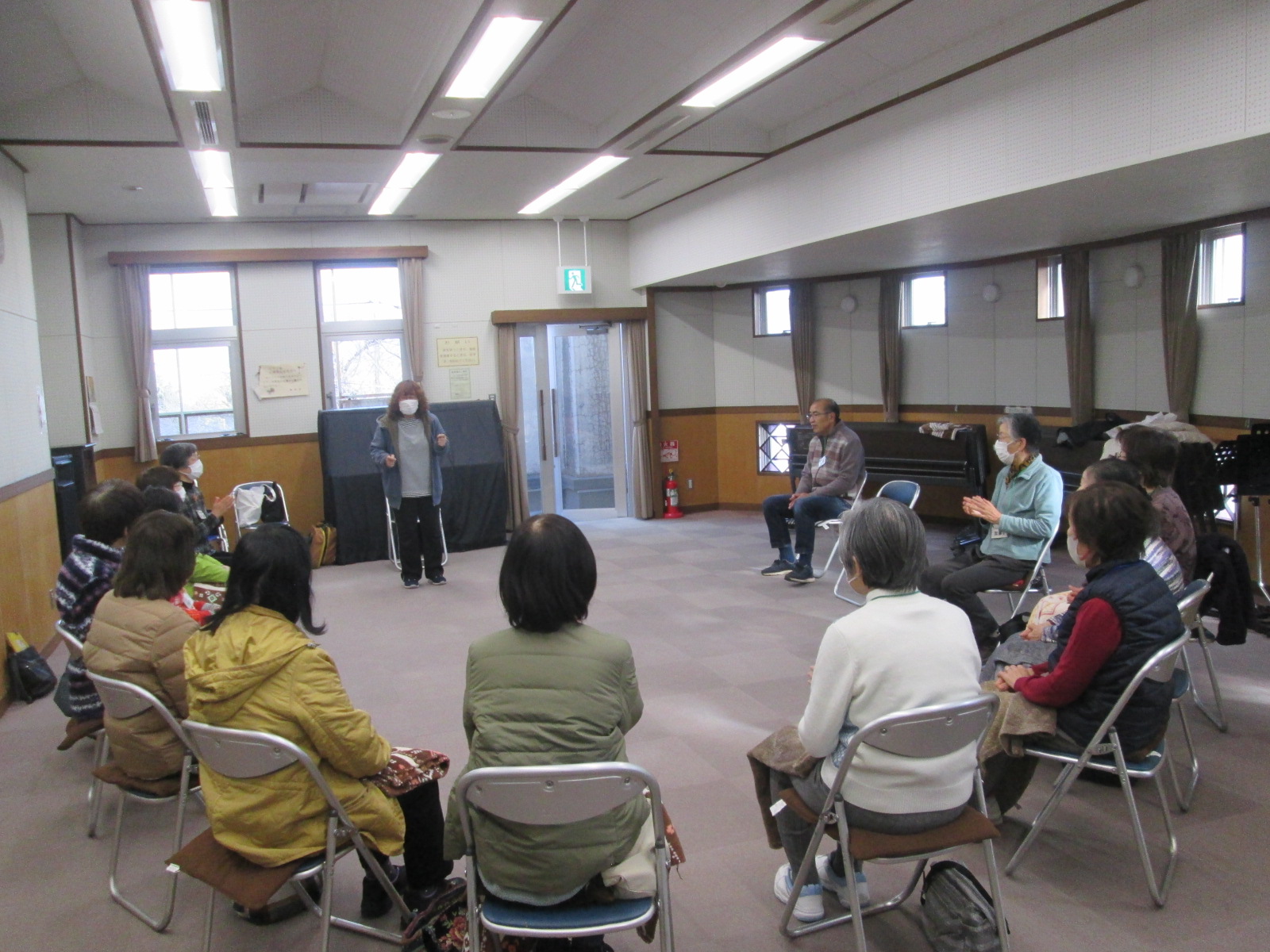 高齢者のグループが赤と青のボールを使ってボッチャのレクリエーション活動をしており、中央の女性が前に歩き出している様子の写真