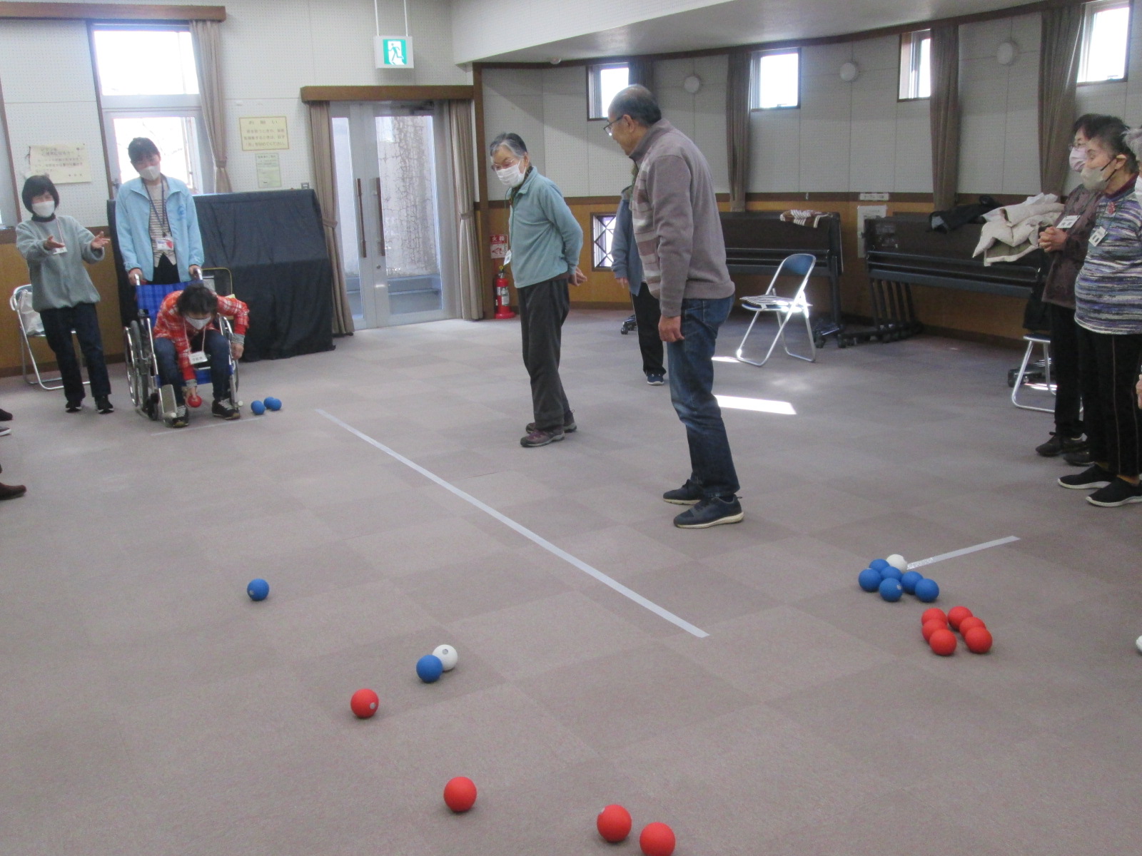 高齢者のグループが赤と青のボールを使ってボッチャのレクリエーション活動をしている様子を捉えた写真