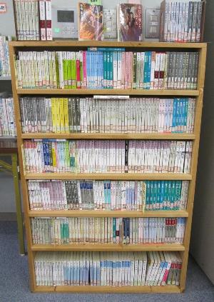 茶色の木製の書棚に、色とりどりの背表紙を持つ文庫本がびっしりと六段にわたって整然と並べられており、一番上の棚上には数冊の新刊らしき本が平積みで展示されている、図書室の風景写真