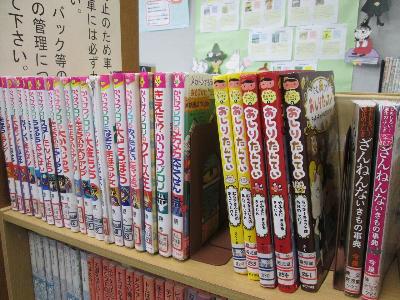 木製の書棚の上段に、「かいけつゾロリ」シリーズや「おしりたんてい」シリーズなどの人気のある児童書や絵本が背表紙を見せて一列に並べられてある図書室の児童書コーナーの写真