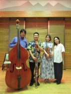 コントラバス、ファゴット、ヴァイオリンを持つ三人の奏者と一人の女性が並び、笑顔でこちらを向いている写真