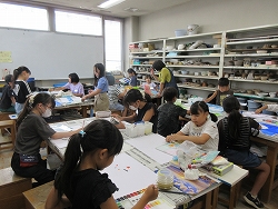 子供たちが棚に作品がたくさん置いてある室内で、絵の具や粘土などを使ってそれぞれ自由に制作活動を楽しんでいる様子の写真