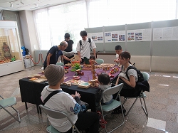 テーブルの上で複数の大人が子供と一緒に木で出来たおもちゃで遊んでおり、周囲には展示パネルが設置している写真