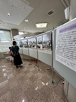 円形に並べられたパネルに古い白黒写真が多数展示され、その隣には展示物の説明が書かれた大きなパネルを親子が見ている様子の写真