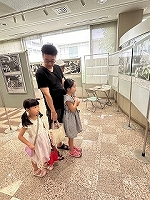 2人の女の子とその父親がパネルに展示してある古い白黒写真を見ている写真