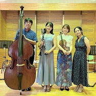 コントラバス、クラリネット、バイオリンの楽器を持った男女4人が立ち並び記念撮影をしている写真