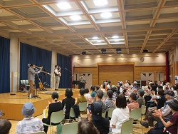 ステージ上で2人のジャズバンドが演奏をし、会場に集まった大勢の観客が拍手を送っている様子の写真