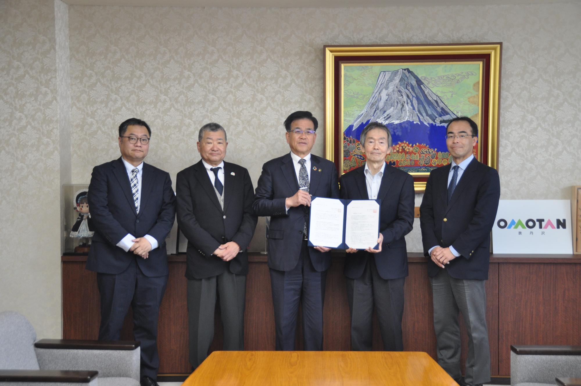 写真：市長（中央）に答申書及び提出文を手渡す坂野会長（右から2人目）と委員（令和8年3月30日市長への答申及び報告会にて）