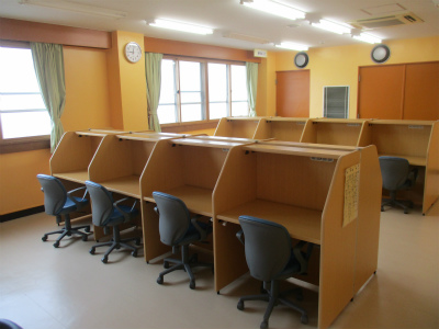 窓際に一列、部屋の奥に一列、明るい木目調の仕切り付きの自習用ブースと青い椅子が並び、静かに勉強に集中できる環境が整えられている学習室の写真