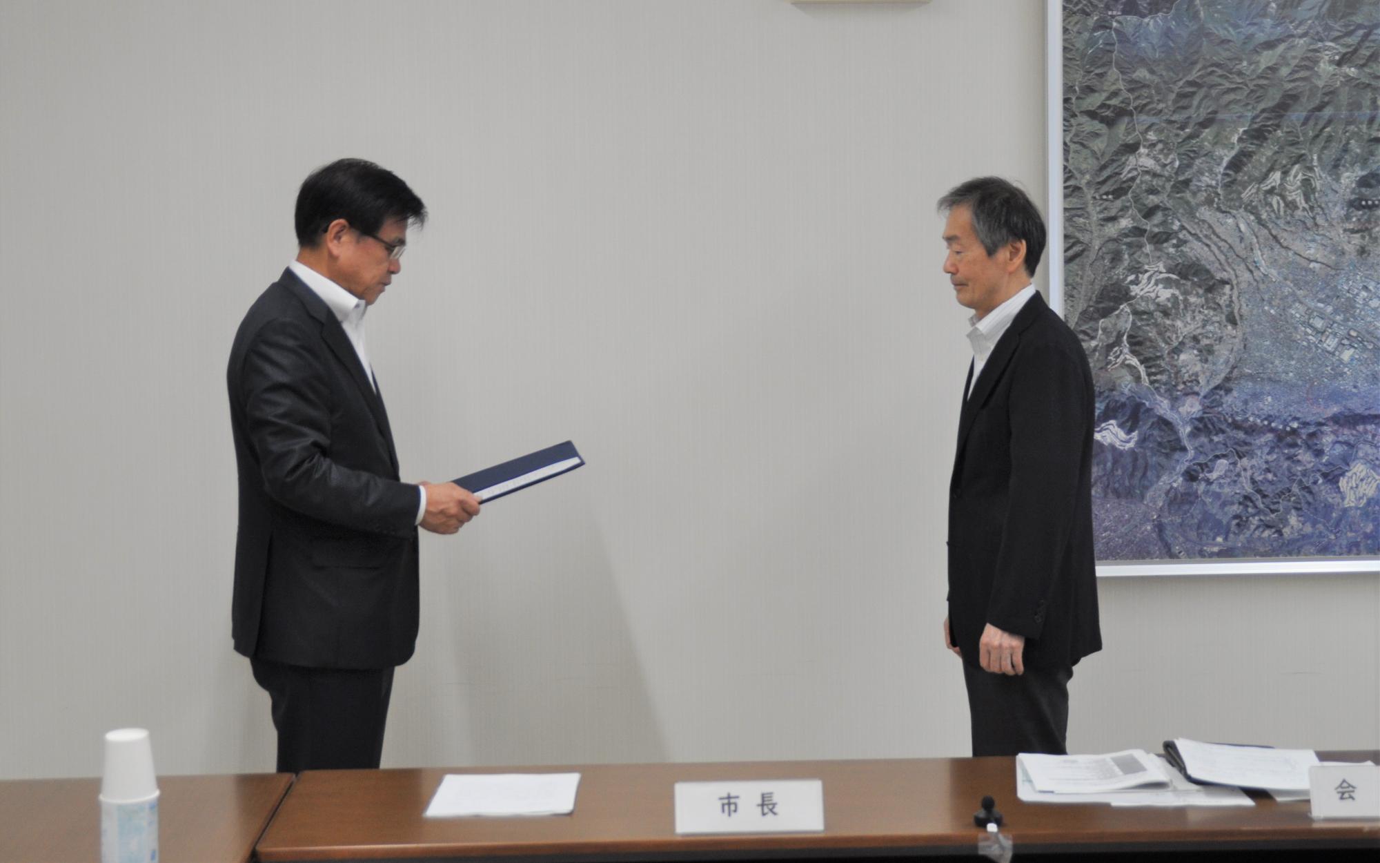 市長が坂野会長に諮問書を手渡そうとしている様子を横向きから撮影した写真