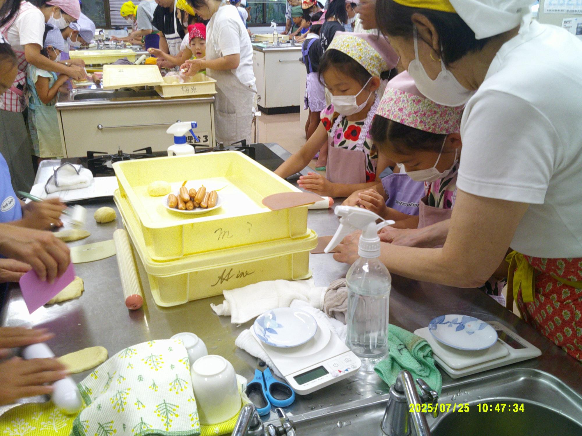 調理場で、三角巾とマスクをつけた親子が、作業台でパン生地をこねている様子の写真