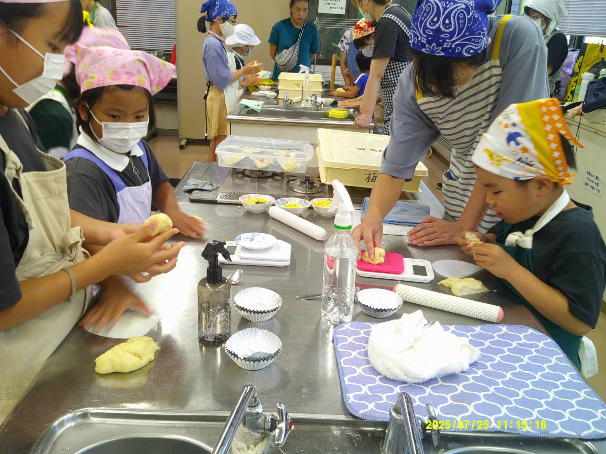 調理台で、エプロン姿の親子連れがパン生地をこねて成形している写真