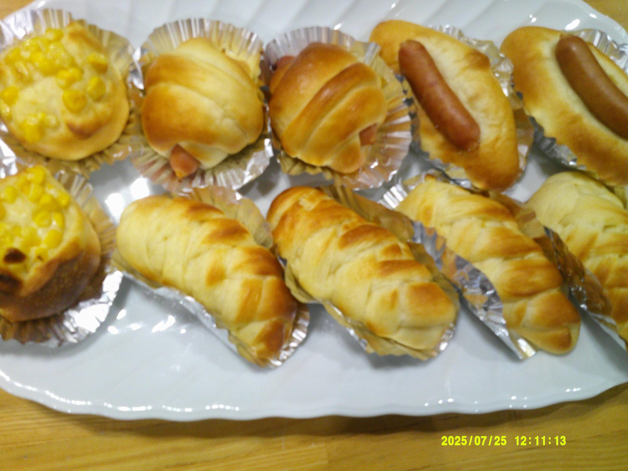 白い楕円形の皿の上に、ウィンナーを巻いたパンとコーンマヨネーズをトッピングして焼かれたパンが、アルミカップに乗せられて並べられている写真