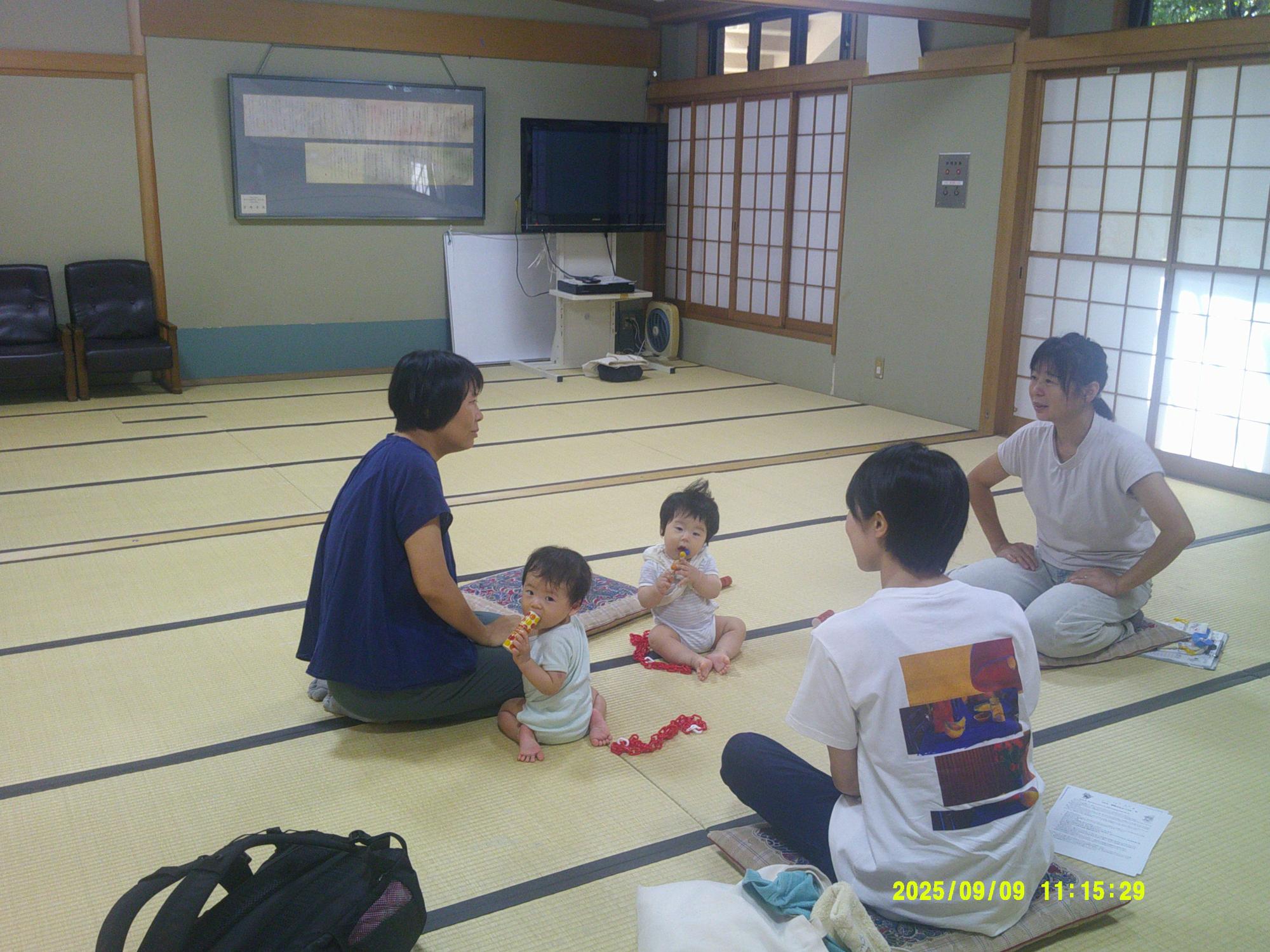 和室の畳の上で女性が3名座っており、床に座って遊ぶ二人の赤ちゃんを囲んで会話をしている写真