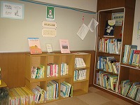 子供向けの本や絵本が並ぶコーナーの棚の前に、壁に張られたポスターや絵が飾られている図書館の一角の写真