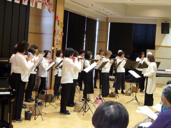 多目的ホールで女性が白のブラウスに黒のズボンをはいたROSEの20人のメンバーによるオカリナ合奏