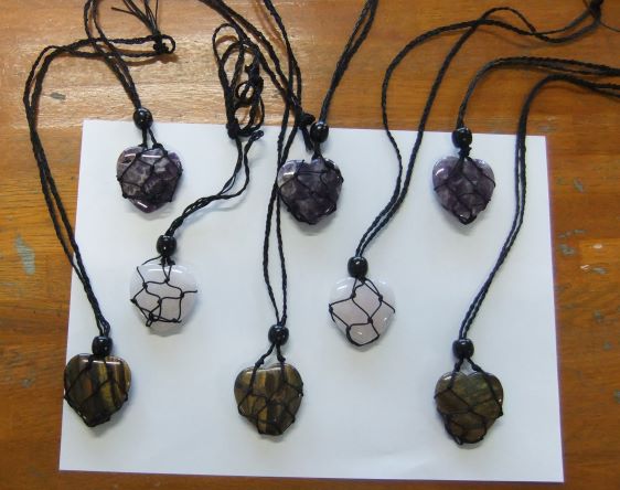 机の上に黒い紐で編んだ中にハートのパワーストーンを入れたキーホルダーを7つ並べて写真