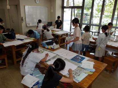 大きな机の前に数名の子どもたちが絵を描いている