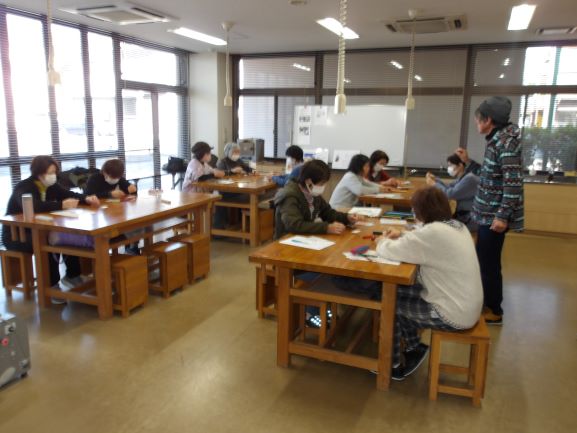 講師一人に10人の参加者が椅子に座りワイヤーアートの作成手順の説明を受けているところ