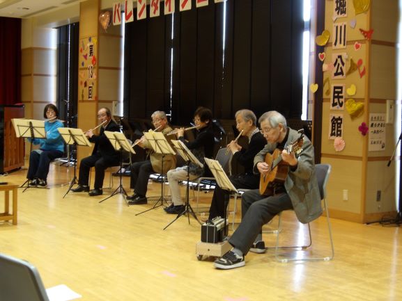 多目的ホールで5人のフルートとギターのアンサンブルを奏でている写真