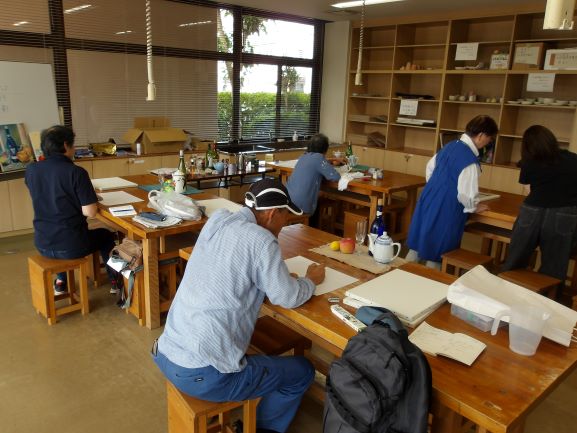 創作活動室の大きな作業台で大人が4人絵を描いている