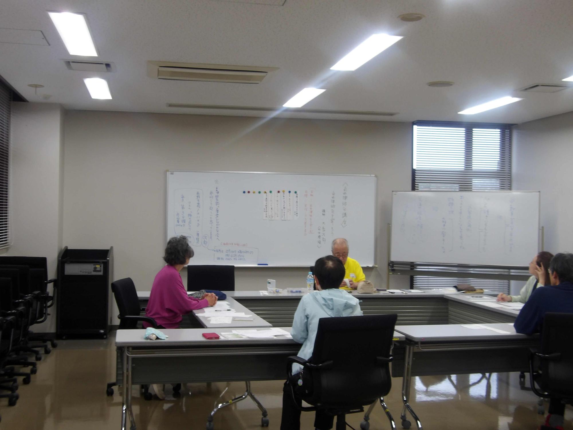 集会室で5人の大人が机を囲み座って講座を受けている