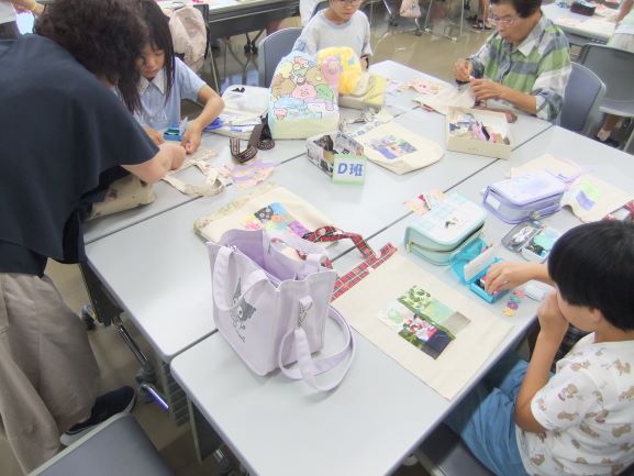 机を囲んで大人と子供が縫い物をしている