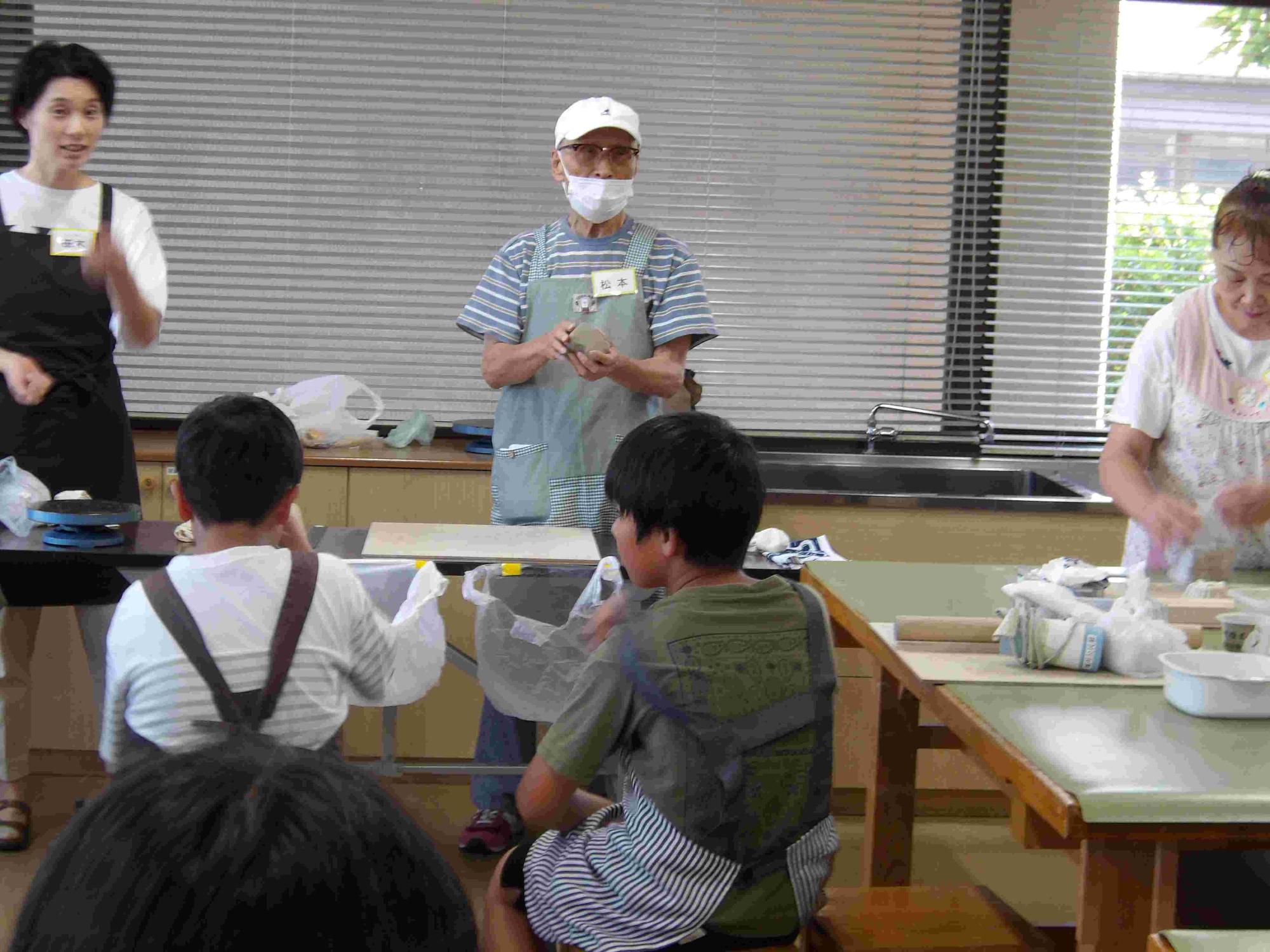 男の人が一人前に立ち数名の子どもたちに陶芸の説明をしている