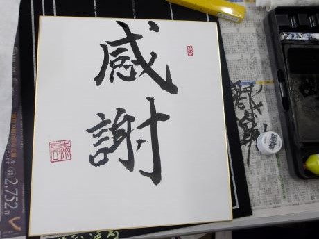 墨で「感謝」という文字が書かれた色紙の横に、硯や落款印、筆が置かれており、書道教室で完成した作品と道具を写した写真