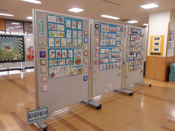 パネルで仕切られた空間に、子どもたちが描いた可愛らしい絵が多数展示されており、右奥の柱には図書館を示す看板がある様子の写真