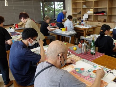 参加者達がそれぞれの席で、机の上に置かれたモチーフや資料を見ながら、水彩画やデッサンに取り組んでいる様子の写真