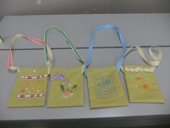 淡い黄緑色の布地に、カラフルなリボンやビーズ、刺繍で可愛らしく装飾が施された四つの手作りミニバッグが並べられている写真