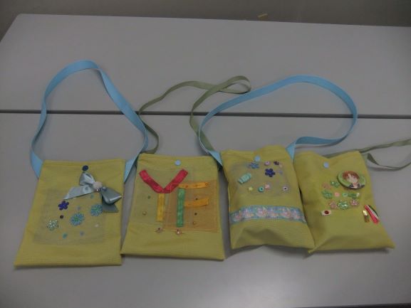 灰色の机の上に並べられた、ストラップの長さや装飾が異なる4つの手作りミニバッグの写真