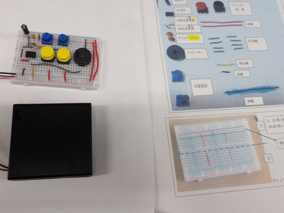 木製の机の上に置かれた、電子部品を組み込んだ白いブレッドボードと黒いケース、そして組み立て方法が図示された説明書が写る写真