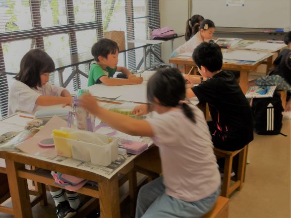 机が複数並んだ教室で、それぞれの机に座って集中して課題に取り組んでいる複数の子供たちを、窓から差し込む光とともに捉えた写真