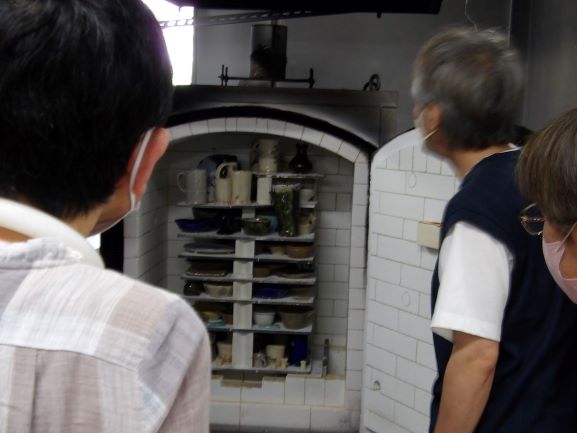 大きな電気窯から焼きあがった様々な陶器を取り出す様子を複数の人が囲んで見つめている写真