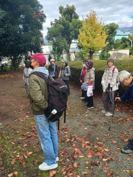 男性一人が前にいてその後ろに数名の女性が公園らしき場所で鳥を観察している