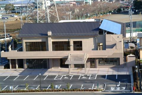 茶色を基調とした二階建ての建物で、中間部分は水平に伸びる庇があり、手前には白線で駐車枠が区切られたアスファルト舗装の広い駐車場がある堀川公民館の外観写真