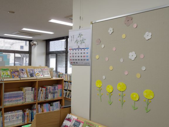 図書室の壁面に黄色の菜の花の貼り絵と花や丸の切りえが貼ってある