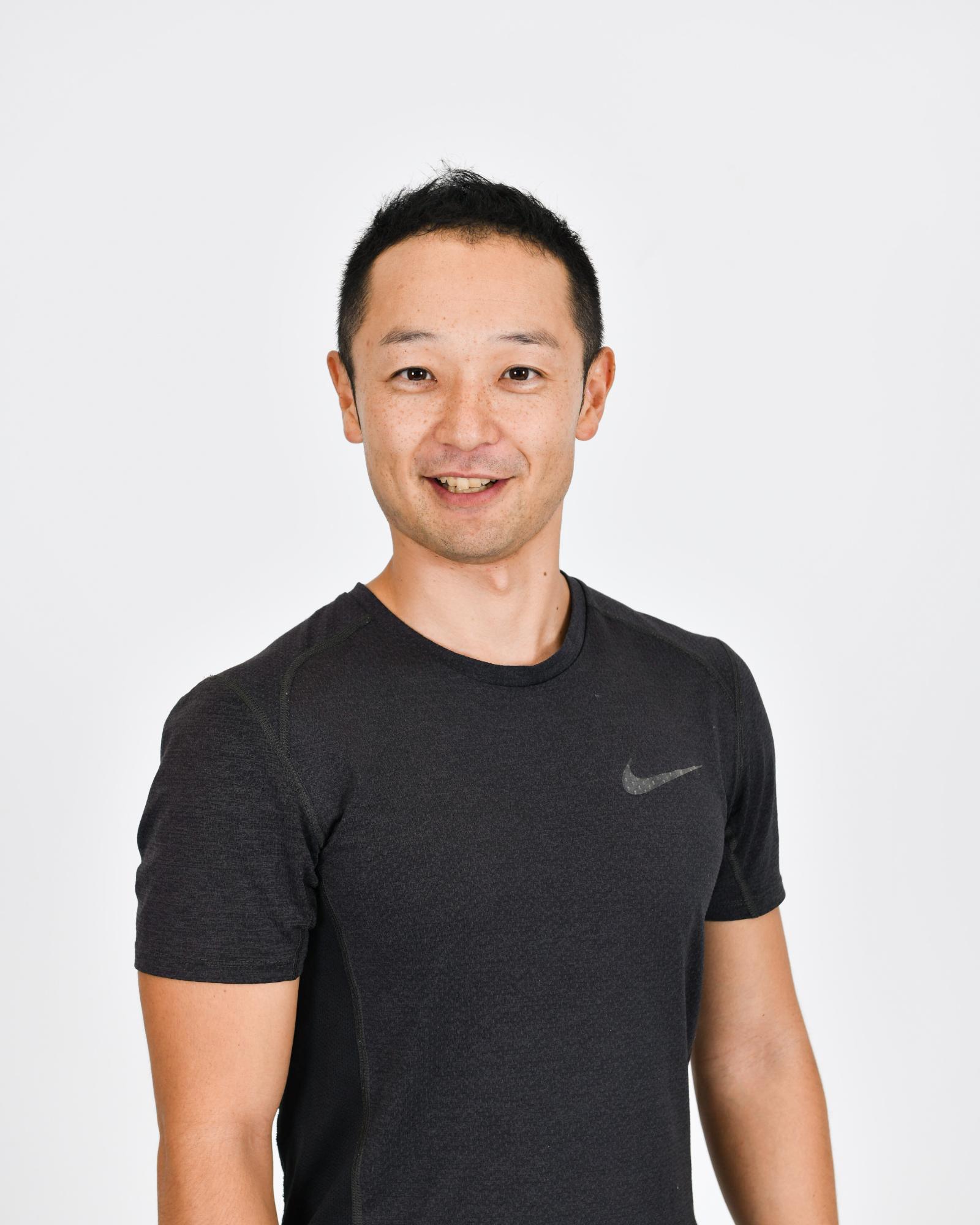 白い背景の前で、短い黒髪の五味宏生さんが濃いグレーのナイキのスポーツTシャツを着用し、カメラに向かって穏やかに微笑んでいる、上半身を写した写真