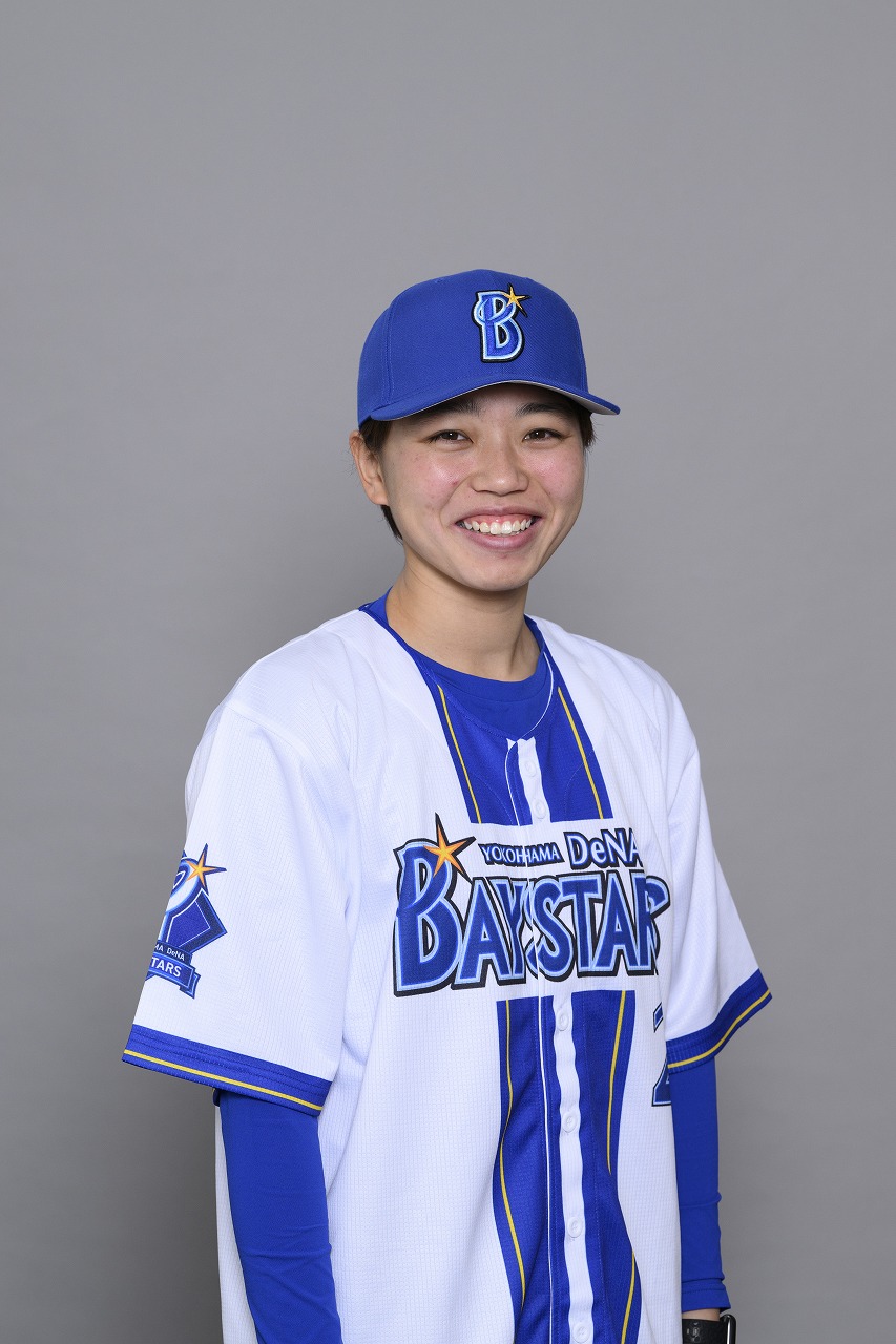 青と白の横浜DeNA BAYSTARSのユニフォームと青いキャップを着用し、青い長袖インナーを着た高橋結央さんが、灰色を背景に正面を向いて明るく微笑んでいる胸上の写真