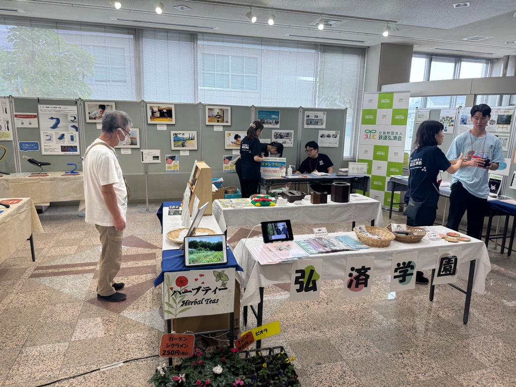 建物の一室で行われている展示会や即売会のようなイベントで、複数のブースが並び、来場者とスタッフが会話を交わしながら商品や展示物を紹介している様子の写真