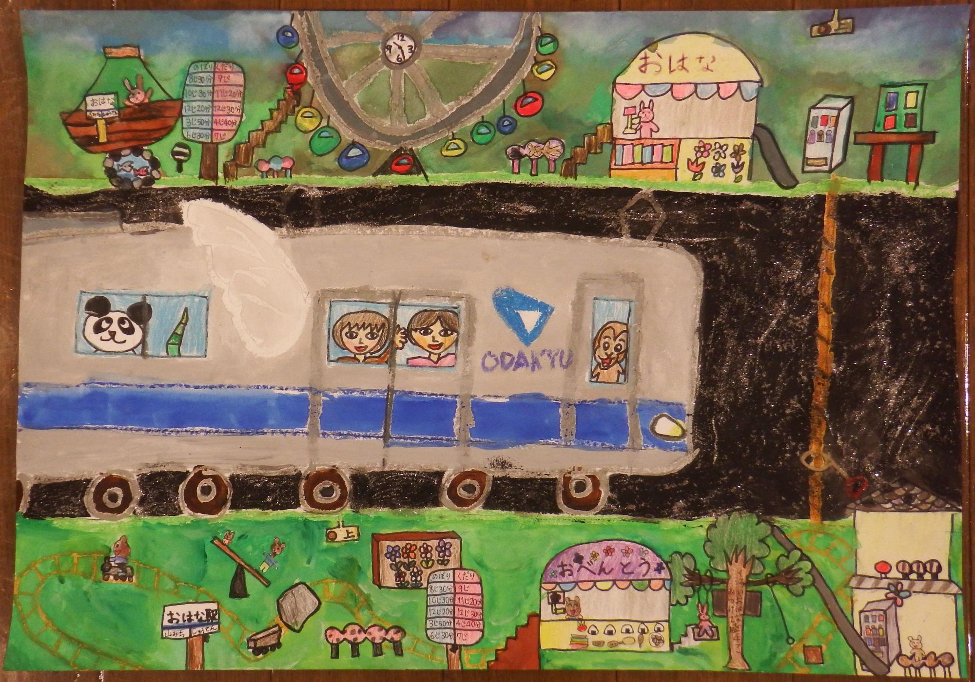 上部には「おはな」と書かれたお花を売っている売店や観覧車、下部にはおにぎりなどを販売している「おべんとう」と書かれた売店やシーソーなどの遊具、「おはな駅」と書かれた駅の看板が設置された遊園地の中を、パンダや笑顔の子供が顔を出した窓と窓の間に羽がついた小田急線のロゴや青いラインの入ったグレー色の電車が走っている様子が描かれた入選受賞作品の写真