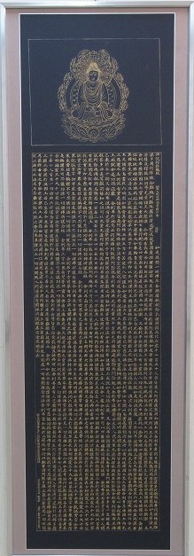 上部には蓮華座に座る金色の仏像が描かれ、その下には金色の文字で経文のようなものがびっしりと書かれている、仏画と経典が描かれた縦長の額縁に入った書道の部で市展大賞を受賞した作品の写真