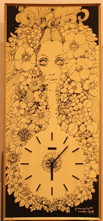 黒色を背景に、豊かなウェーブのかかった髪と、多数の様々な種類の花で囲まれた中央に、はっきりとした顔立ちの女性の顔が描かれ、胸元には花をデザインした文字盤と短針と長針を備えた時計が配された線画作品の写真