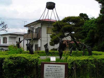 生垣に囲まれた中に設置された、重い槌を滑車で吊り上げては落とす地固めの作業を複数の人物で象ったブロンズ像の写真