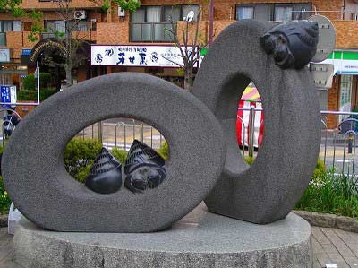 正面と斜めに設置された中心に穴が空いた二つの大きな石の輪に、ヤドカリを思わせる黒い石のオブジェが配置された抽象的な屋外彫刻の写真