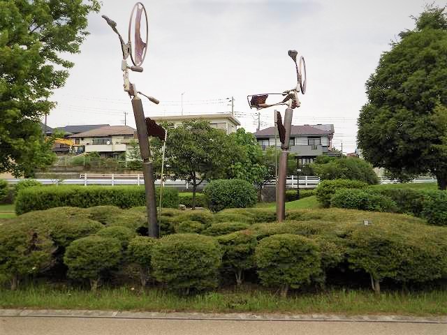 密集した小さな植え込みの中に、2本のステンレス製の棒の上に、円形の金属片が溶接された、一対の奇妙な形状をした抽象的な現代彫刻の写真