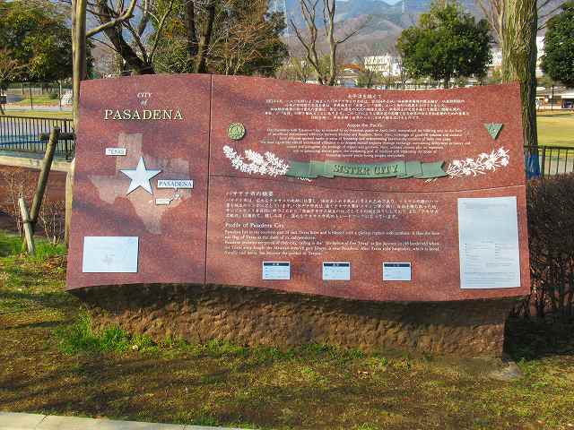 背景に木々が立っている公園内に、英語と日本語の文章や、地図の上に星のマークがデザインされているテキサス州パサデナ市と秦野市の姉妹都市提携を示す説明板の写真