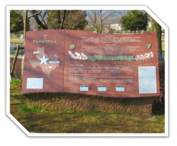 背景に木々が立っている公園内に、英語と日本語の文章や、地図の上に星のマークがデザインされているテキサス州パサデナ市と秦野市の姉妹都市提携を示す説明板の写真